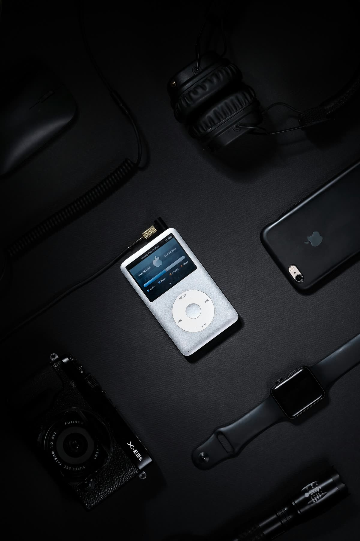 A flat lay of gadgets from different eras: an MP3 player, phone, headphones, watch, and camera